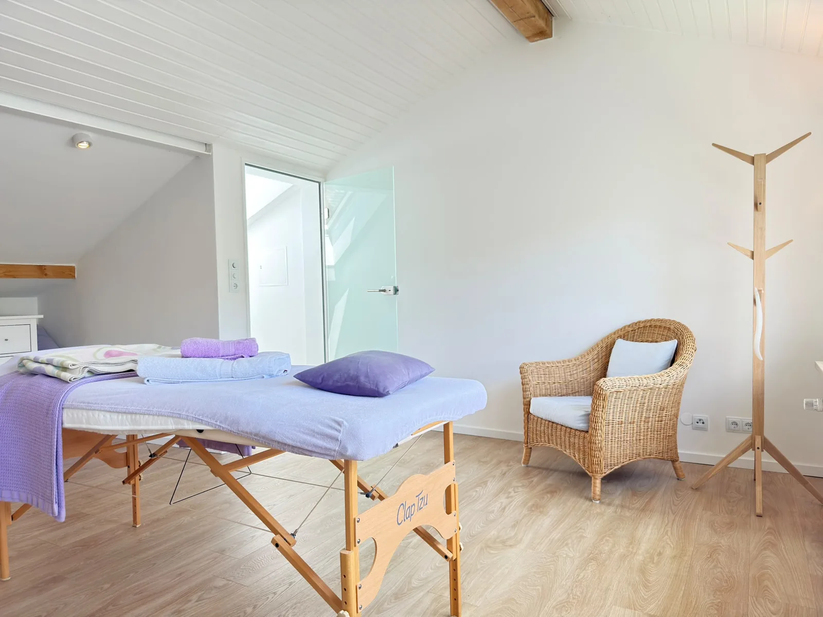Massageliege mit lavendelfarbenen Textilien und Sitzplatz im Behandlungsraum