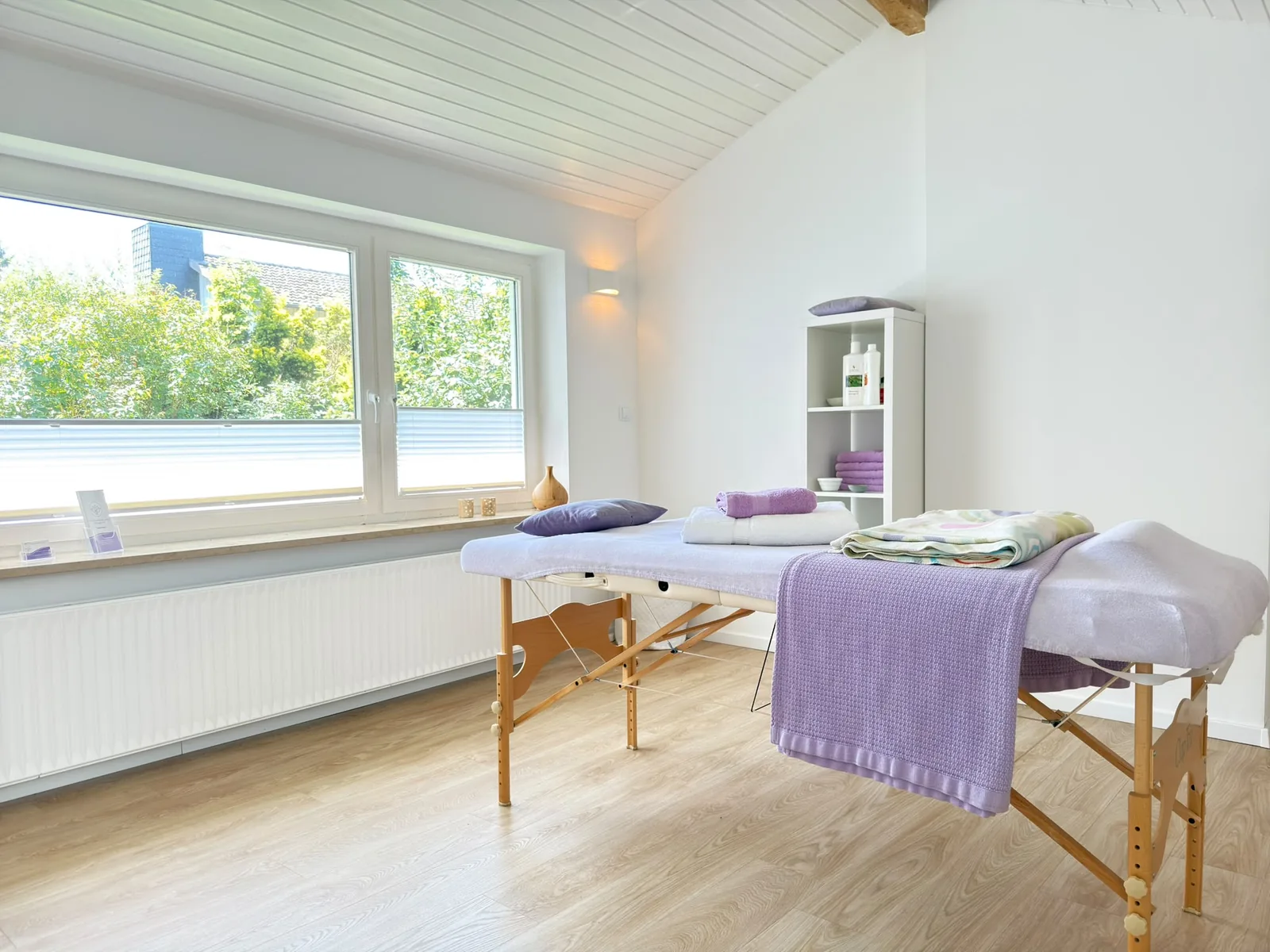 Massageliege mit lavendelfarbenen Handtüchern im hellen Praxisraum